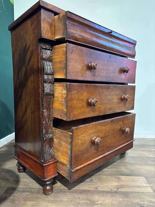 fig 4. A Victorian mahogany chest of drawers featuring carved pilasters, three main drawers with turned wooden handles, a coved top drawer, and bun feet.