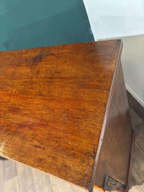 fig 5. A Victorian mahogany chest of drawers featuring carved pilasters, three main drawers with turned wooden handles, a coved top drawer, and bun feet.
