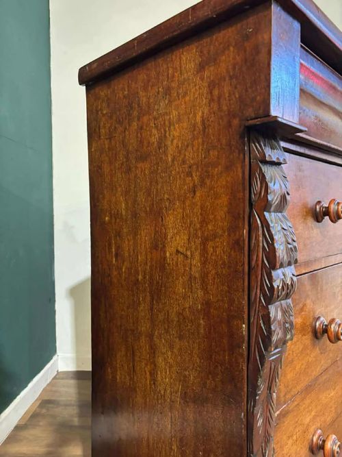 fig 6. A Victorian mahogany chest of drawers featuring carved pilasters, three main drawers with turned wooden handles, a coved top drawer, and bun feet.