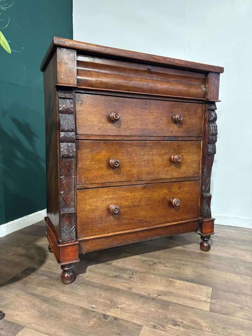 fig 7. A Victorian mahogany chest of drawers featuring carved pilasters, three main drawers with turned wooden handles, a coved top drawer, and bun feet.