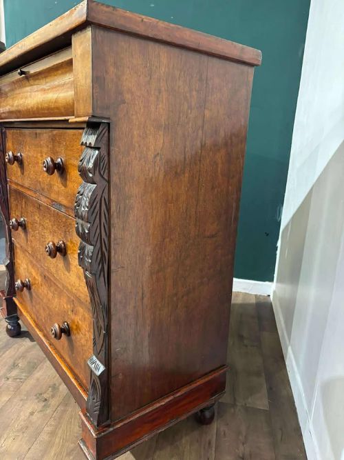 fig 9. A Victorian mahogany chest of drawers featuring carved pilasters, three main drawers with turned wooden handles, a coved top drawer, and bun feet.