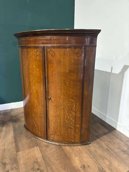 fig 1. A George III oak and mahogany bow-fronted corner cupboard featuring twin curved doors with inlay detail and a moulded cornice.