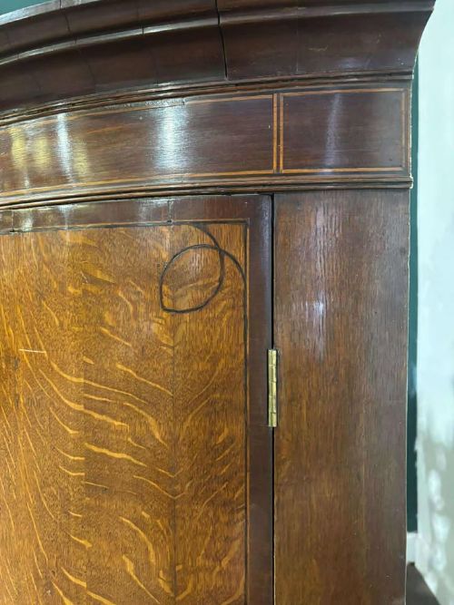 fig 4. A George III oak and mahogany bow-fronted corner cupboard featuring twin curved doors with inlay detail and a moulded cornice.
