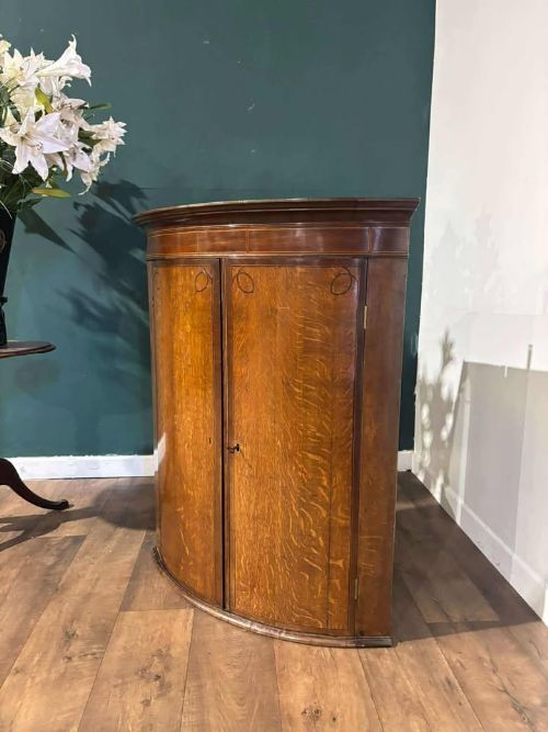 fig 5. A George III oak and mahogany bow-fronted corner cupboard featuring twin curved doors with inlay detail and a moulded cornice.