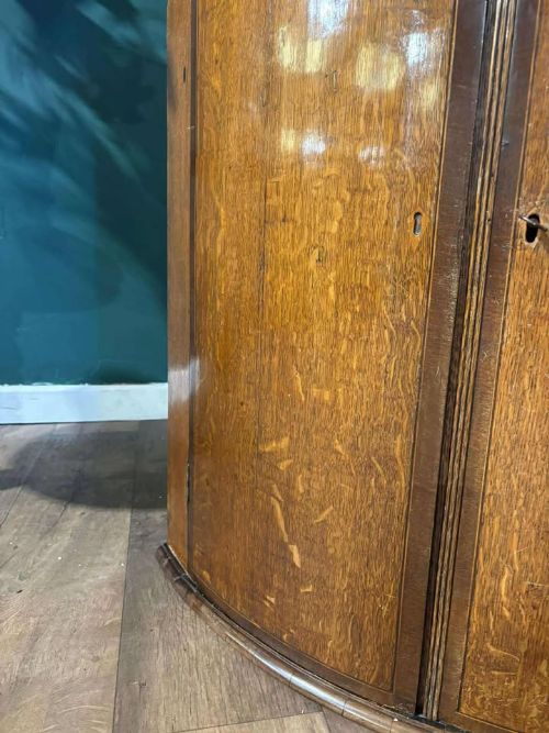 fig 6. A George III oak and mahogany bow-fronted corner cupboard featuring twin curved doors with inlay detail and a moulded cornice.