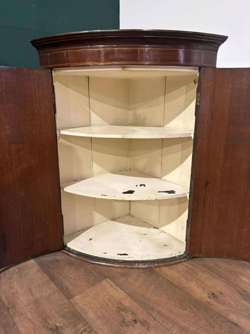 fig 8. A George III oak and mahogany bow-fronted corner cupboard featuring twin curved doors with inlay detail and a moulded cornice.