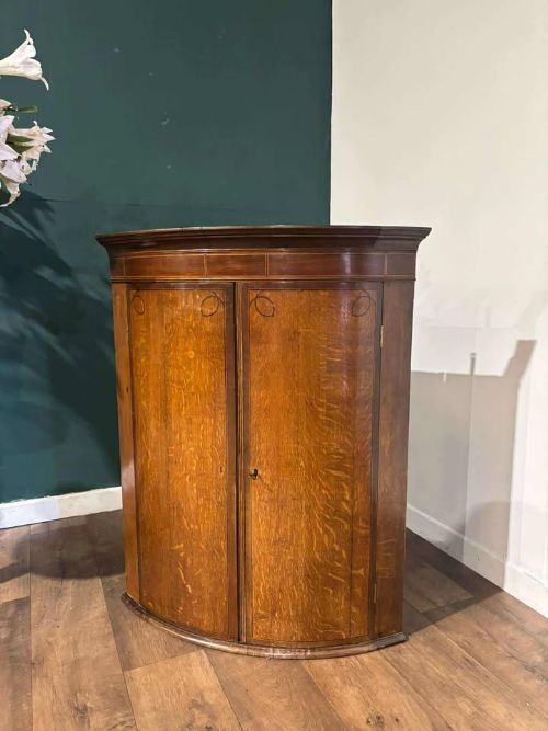 fig 9. A George III oak and mahogany bow-fronted corner cupboard featuring twin curved doors with inlay detail and a moulded cornice.
