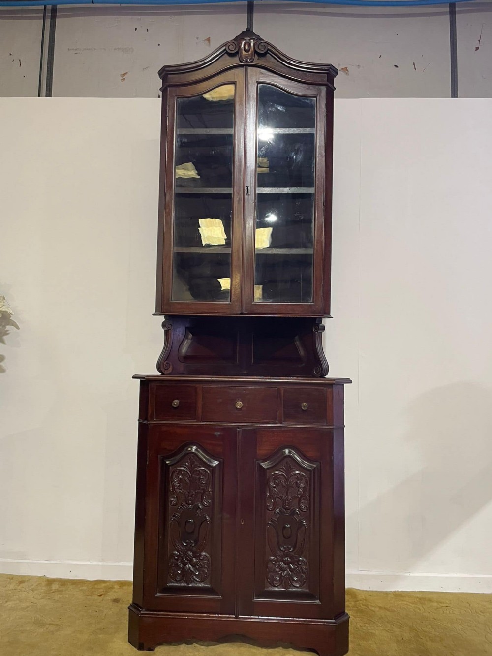 A tall, dark mahogany late 19th-century corner cupboard featuring a glazed upper display cabinet, an open central gallery, and carved lower panel doors.