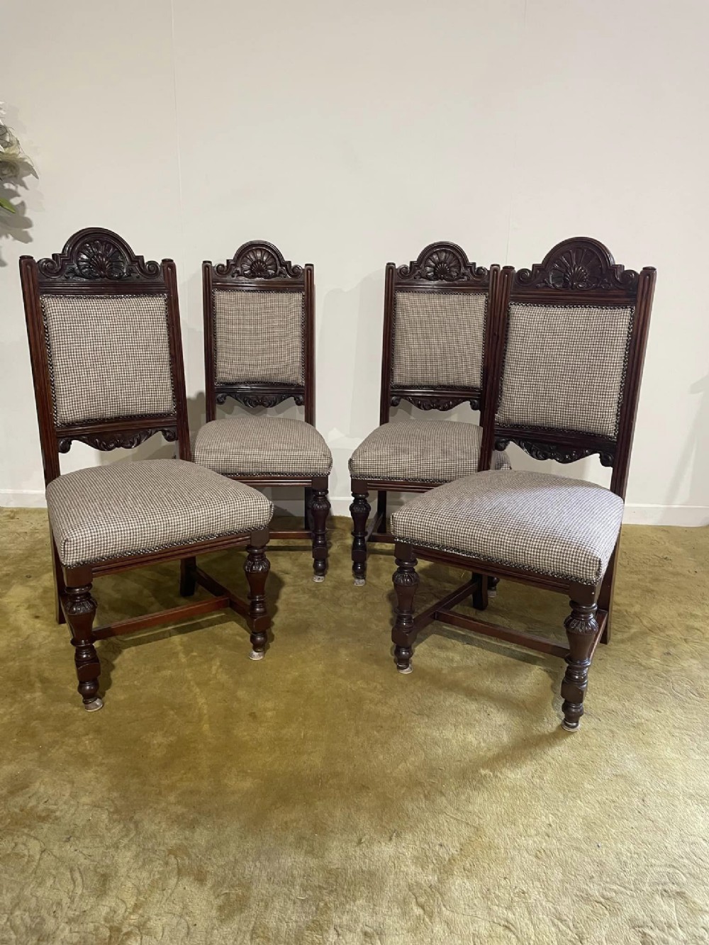 A set of four dark timber Victorian dining chairs featuring carved shell crests, turned front legs, and patterned houndstooth fabric upholstery.