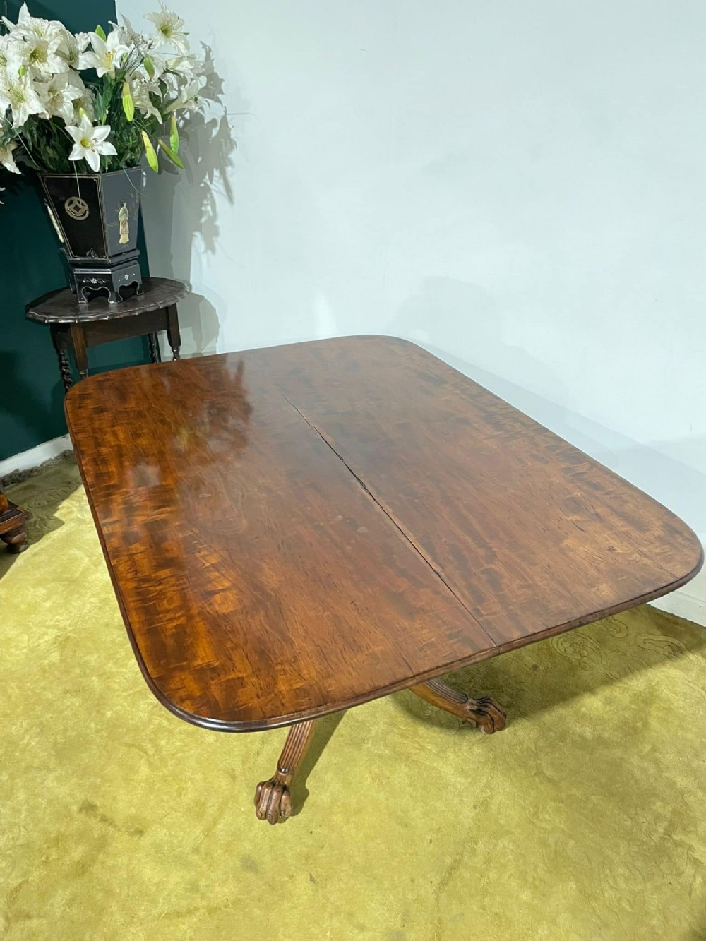 A late Regency mahogany tilt-top breakfast table featuring a rectangular polished top with rounded corners, supported by a central pedestal and reeded quadruped legs with brass paw feet.