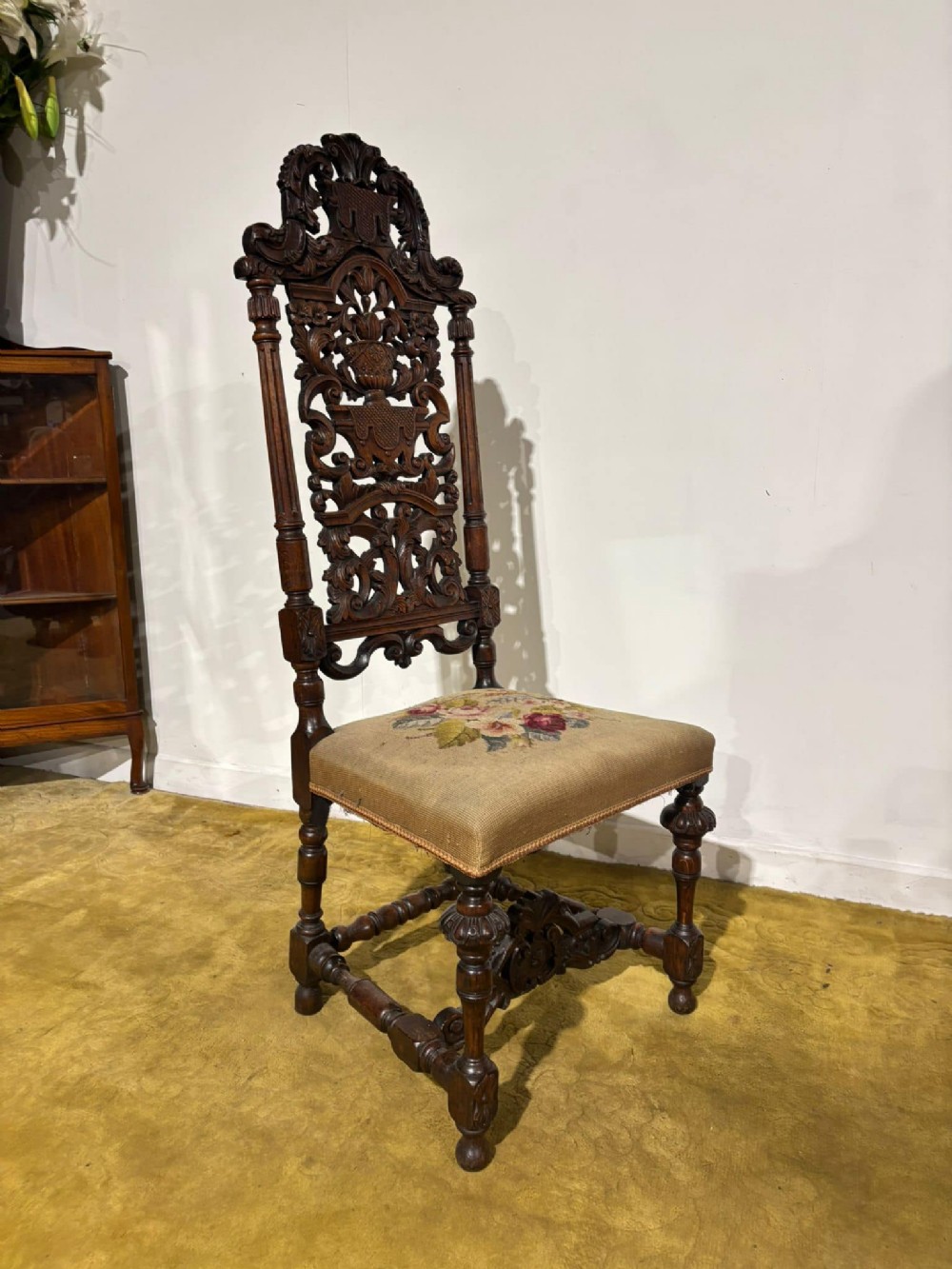 A Carolean carved oak high back side chair featuring an intricately carved foliage cresting, turned supports, and a floral needlepoint seat.