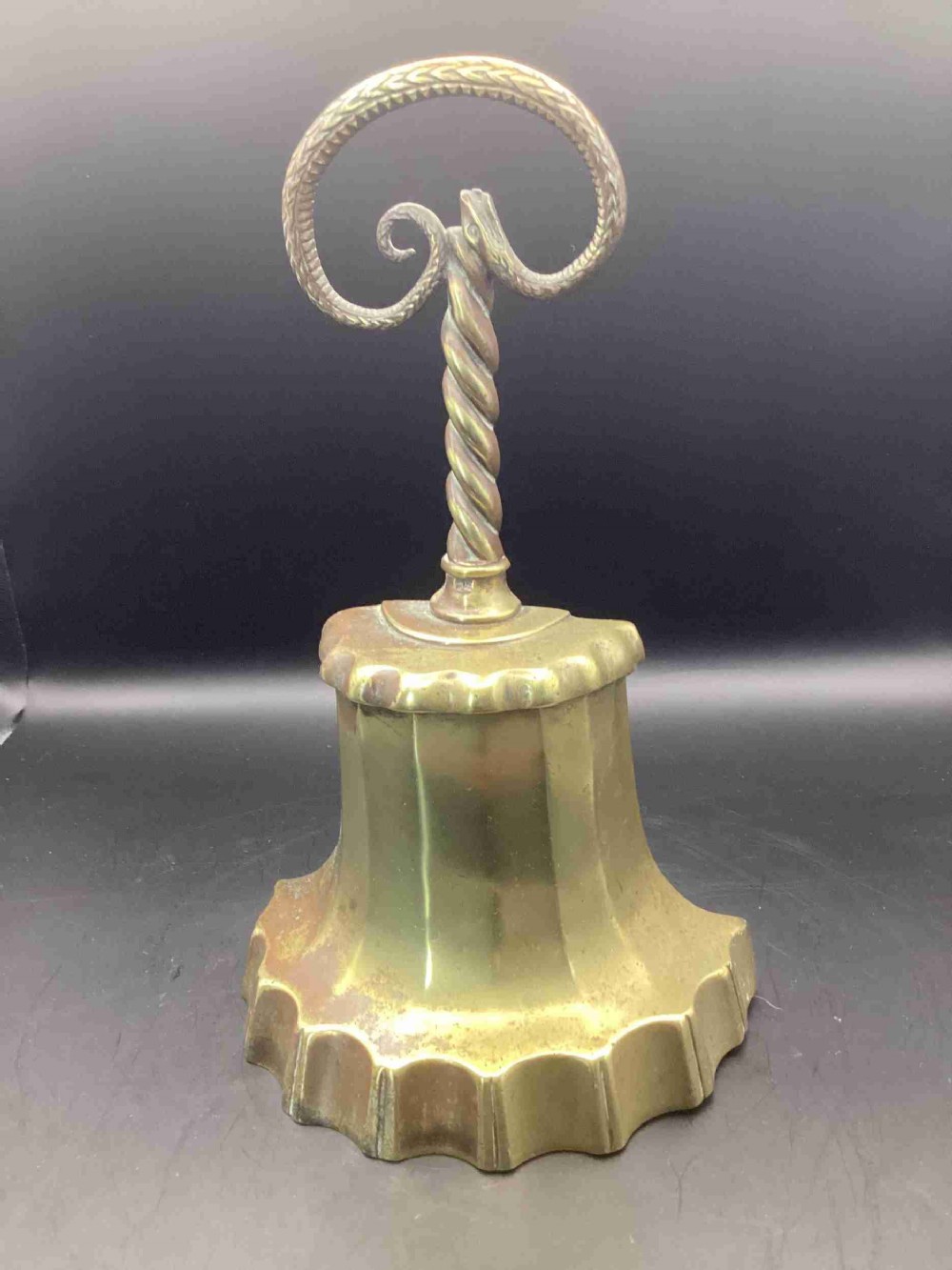 A heavy Victorian cast brass doorstop featuring a scalloped fluted base, a spiral twist stem, and a handle shaped as two looped serpents.