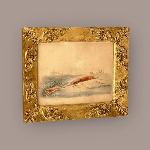 fig 1. A 19th-century watercolour painting depicting two greyhounds pursuing a hare across a field, housed in a wide, ornate gilt frame with acanthus corner details.