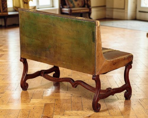fig 1. An antique French leather banquette featuring patinated brown leather upholstery with two vertical velvet decorative bands, supported by a carved wooden base with scrolled legs.