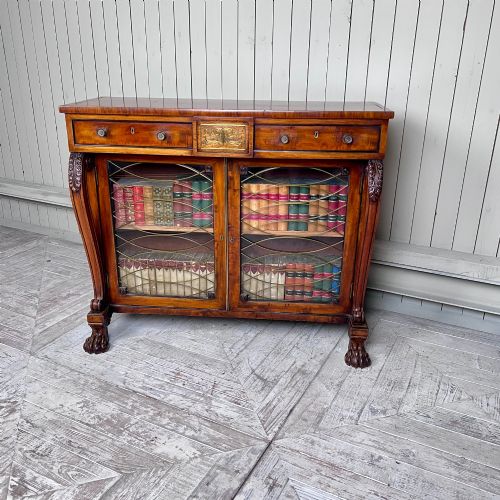 fig 1. A Regency mahogany low chiffonier bookcase featuring brass wire grille doors, carved scroll supports terminating in paw feet, and brass inlay.
