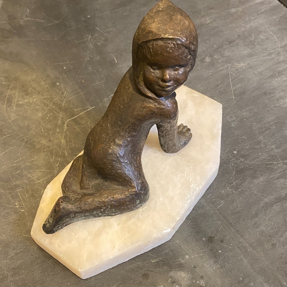 A small patinated bronze figurine depicting a crawling child wearing a bonnet, mounted on a hexagonal white alabaster base. View II