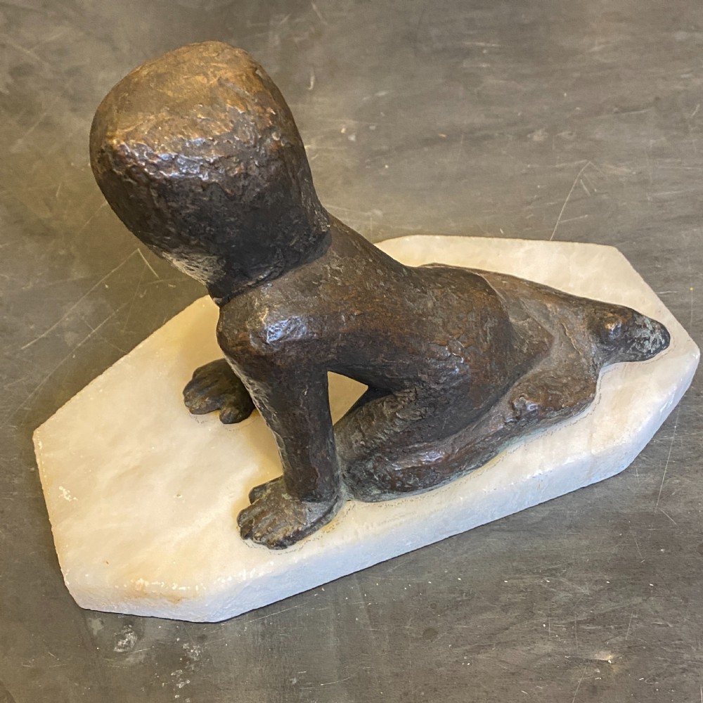 A small patinated bronze figurine depicting a crawling child wearing a bonnet, mounted on a hexagonal white alabaster base. View IV