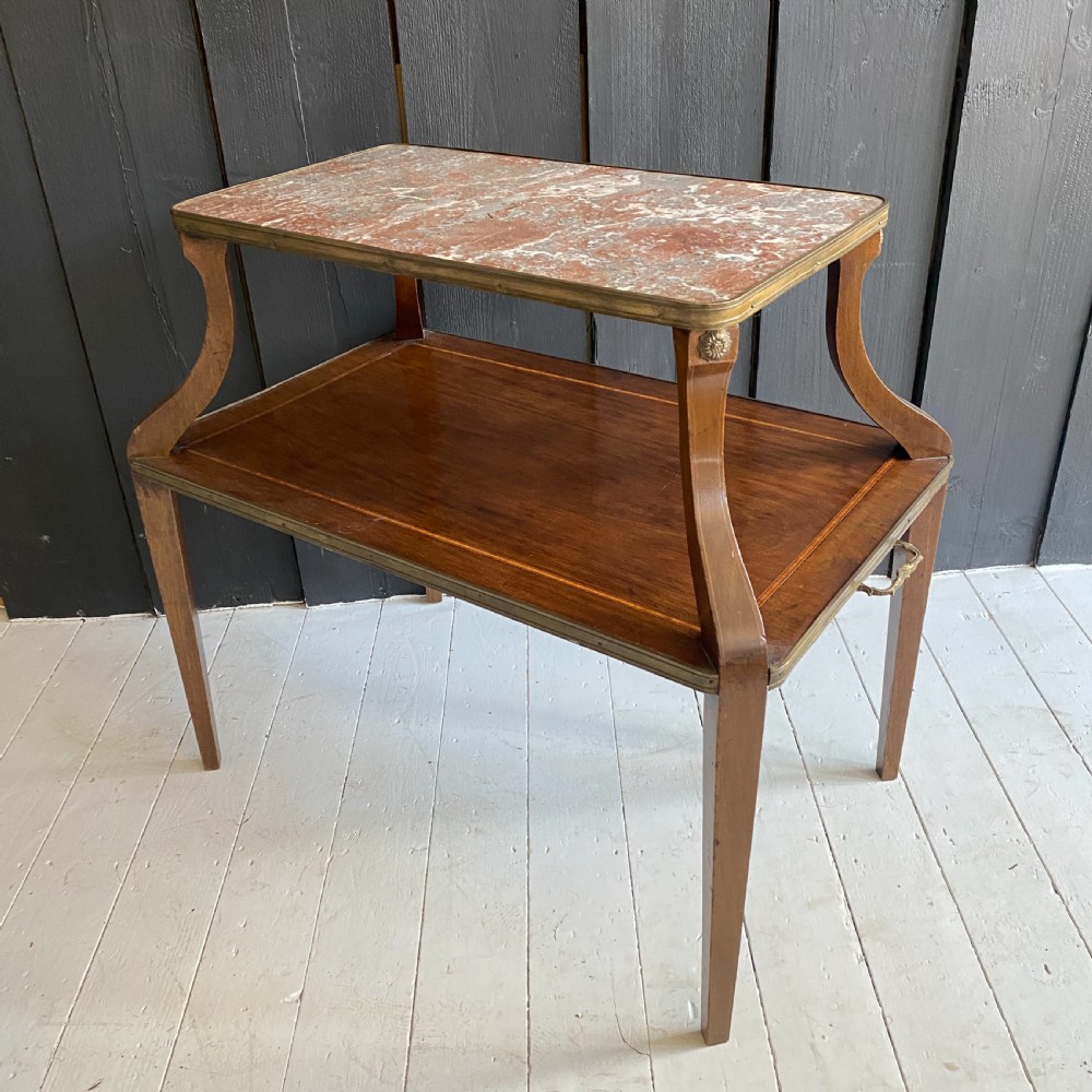 A two-tiered mahogany side table featuring a pink-veined marble top framed in brass, supported by curved legs over a lower wood shelf with brass side handles.