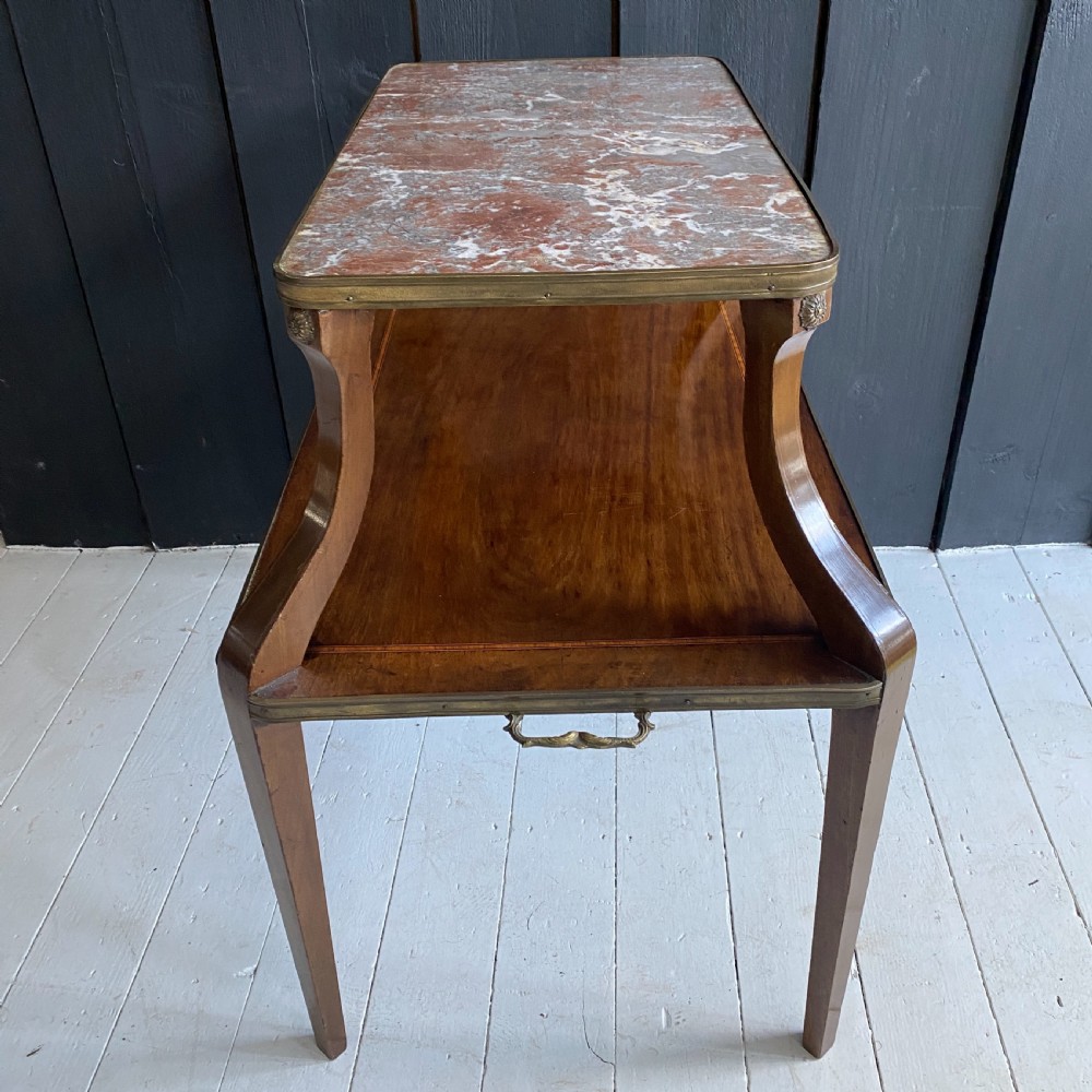 A two-tiered mahogany side table featuring a pink-veined marble top framed in brass, supported by curved legs over a lower wood shelf with brass side handles. View VI