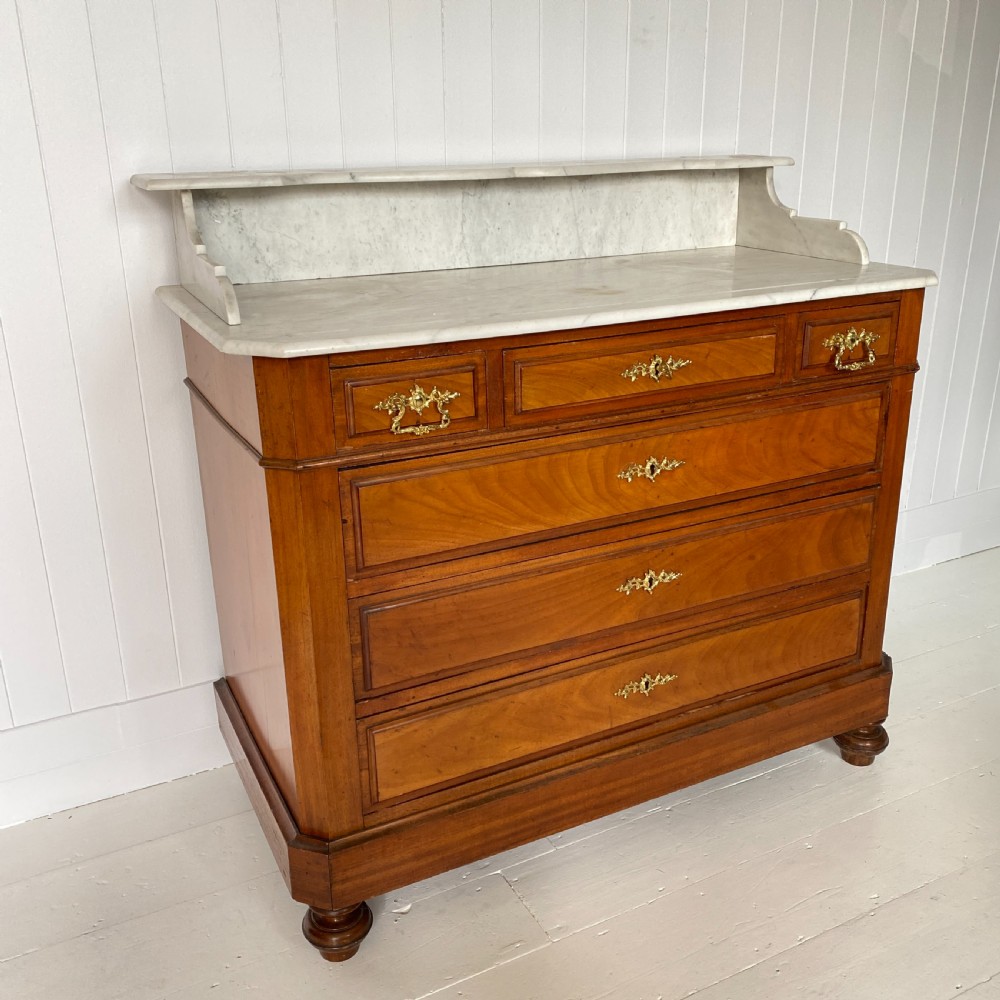 A 19th-century French walnut commode featuring four drawers, decorative brass handles, turned feet, and a white marble top with an upper marble shelf.