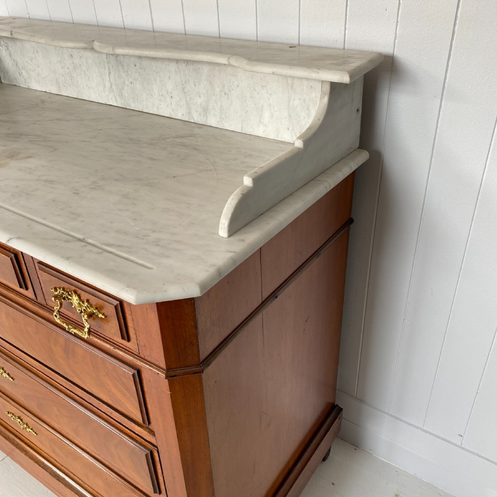A 19th-century French walnut commode featuring four drawers, decorative brass handles, turned feet, and a white marble top with an upper marble shelf. View II