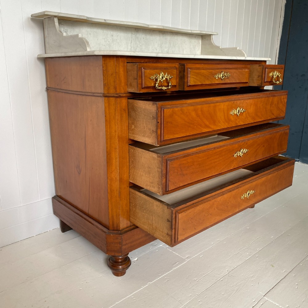 A 19th-century French walnut commode featuring four drawers, decorative brass handles, turned feet, and a white marble top with an upper marble shelf. View IV