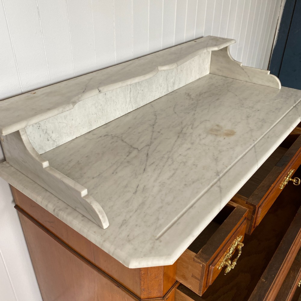 A 19th-century French walnut commode featuring four drawers, decorative brass handles, turned feet, and a white marble top with an upper marble shelf. View V