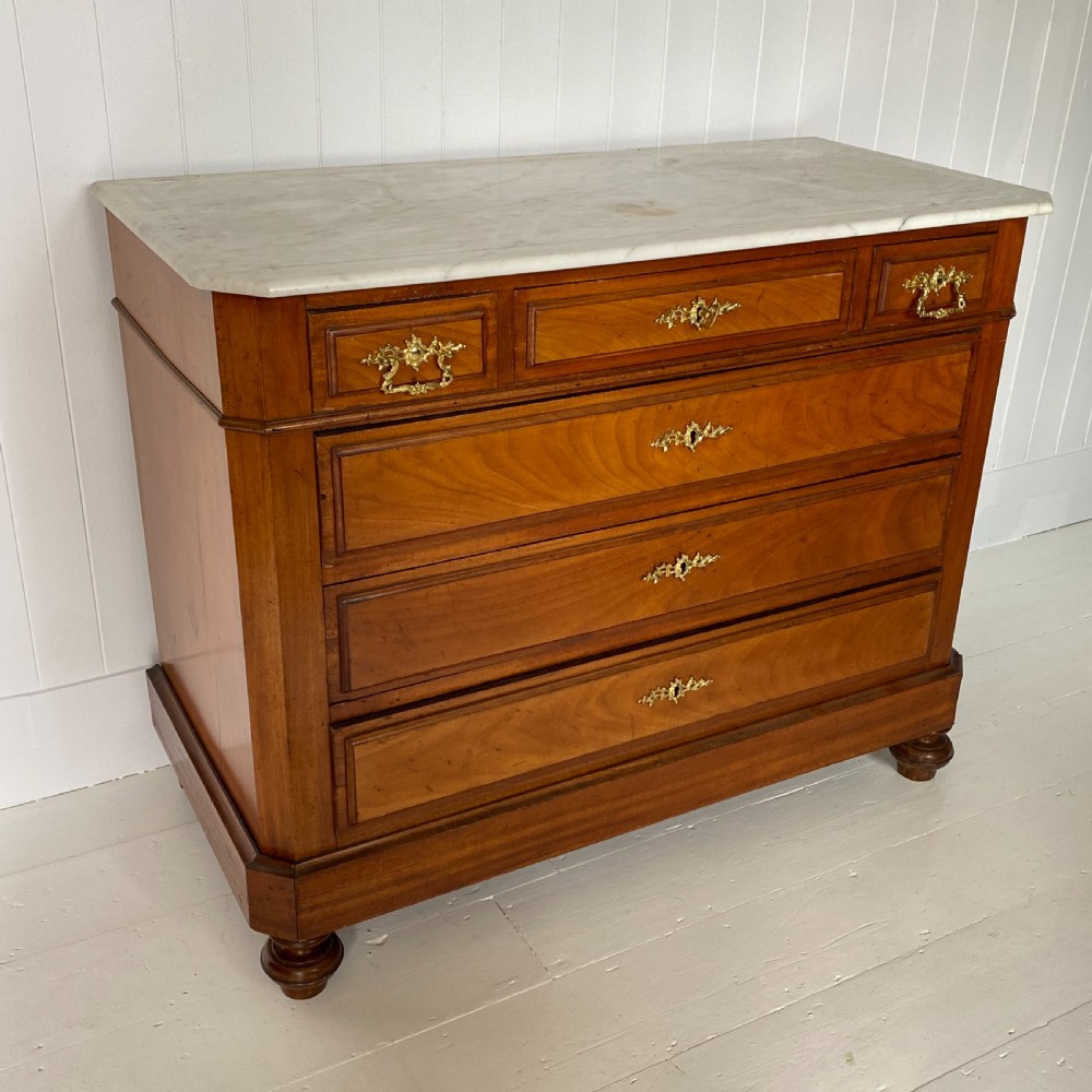 A 19th-century French walnut commode featuring four drawers, decorative brass handles, turned feet, and a white marble top with an upper marble shelf. View VI