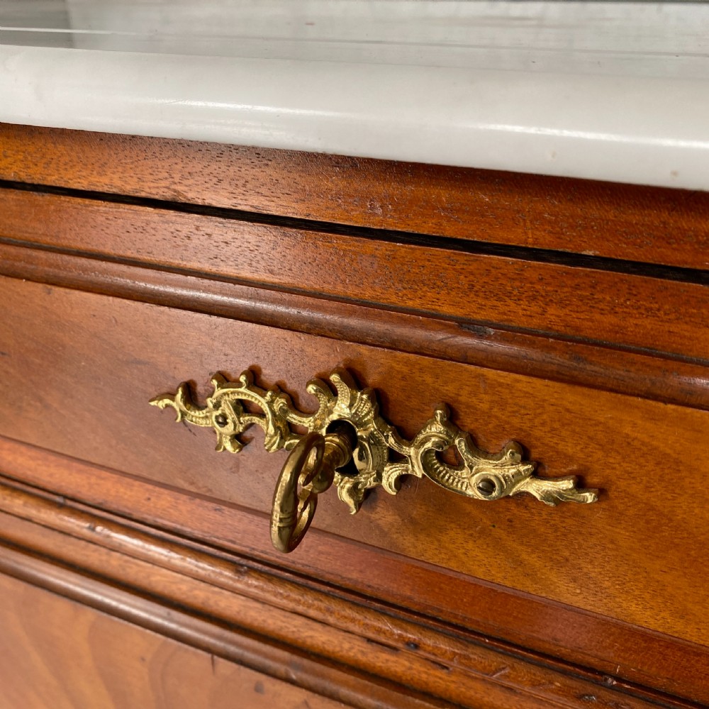 A 19th-century French walnut commode featuring four drawers, decorative brass handles, turned feet, and a white marble top with an upper marble shelf. View VII