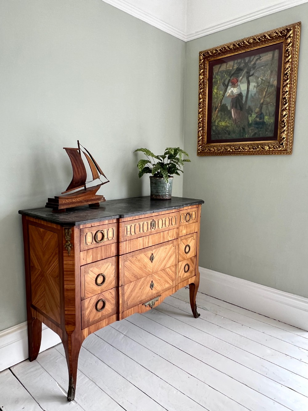 An antique Continental parquetry wooden commode featuring geometric wood inlays, brass ring handles, and a dark grey marble top.