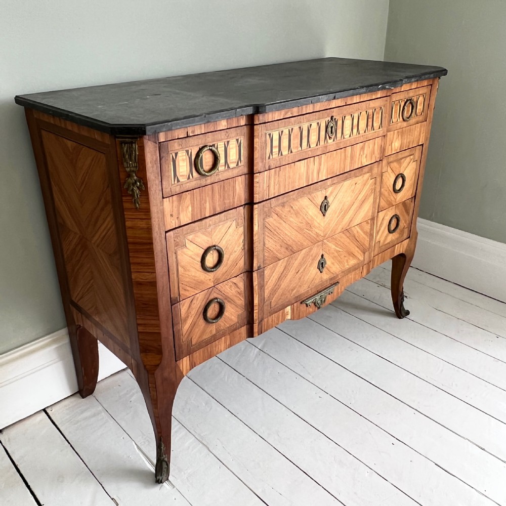 An antique Continental parquetry wooden commode featuring geometric wood inlays, brass ring handles, and a dark grey marble top. View II