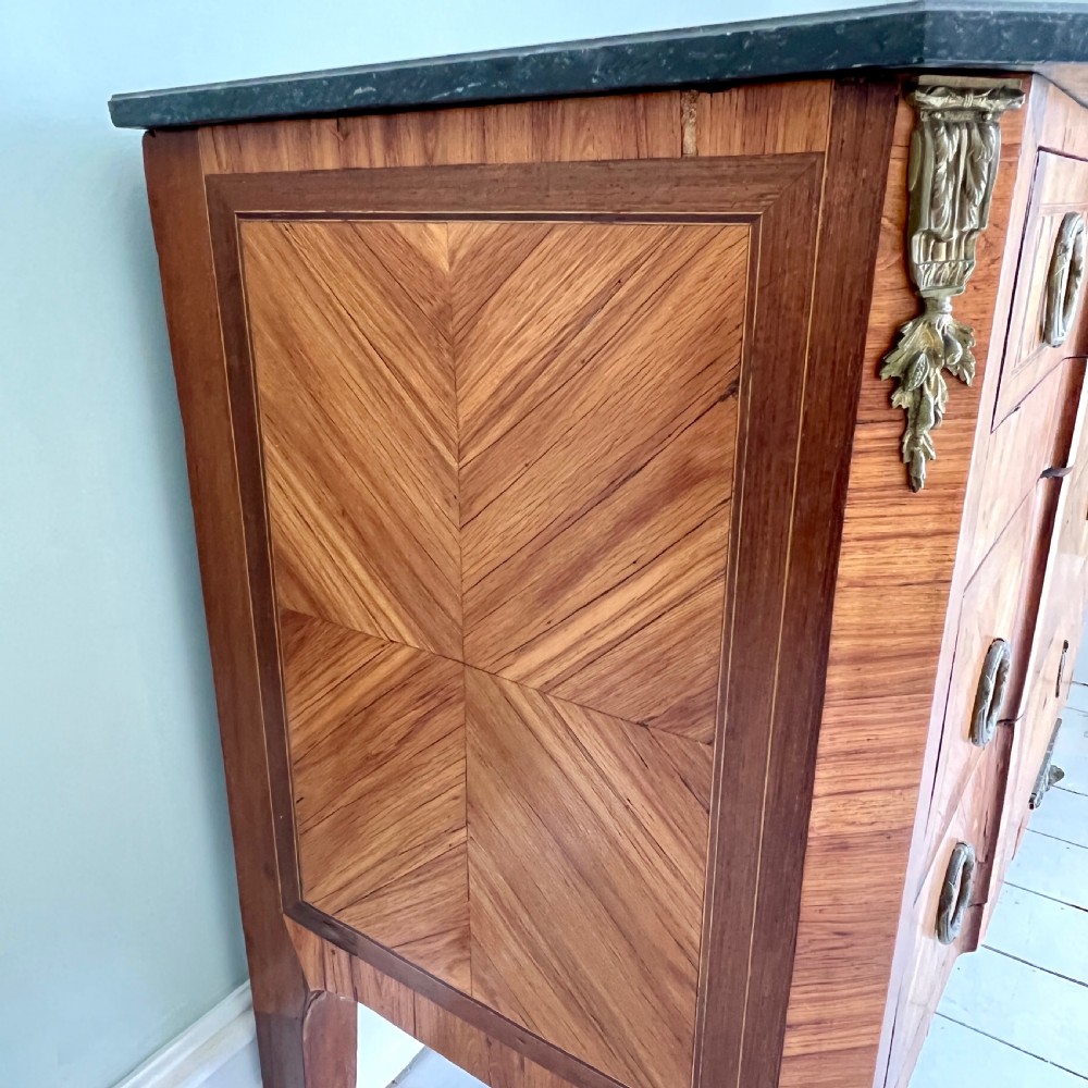 An antique Continental parquetry wooden commode featuring geometric wood inlays, brass ring handles, and a dark grey marble top. View V