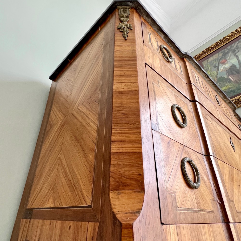 An antique Continental parquetry wooden commode featuring geometric wood inlays, brass ring handles, and a dark grey marble top. View VI