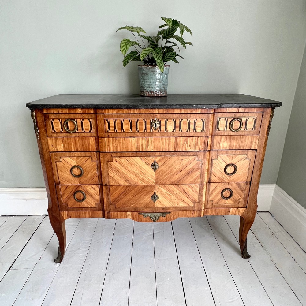 An antique Continental parquetry wooden commode featuring geometric wood inlays, brass ring handles, and a dark grey marble top. View VII