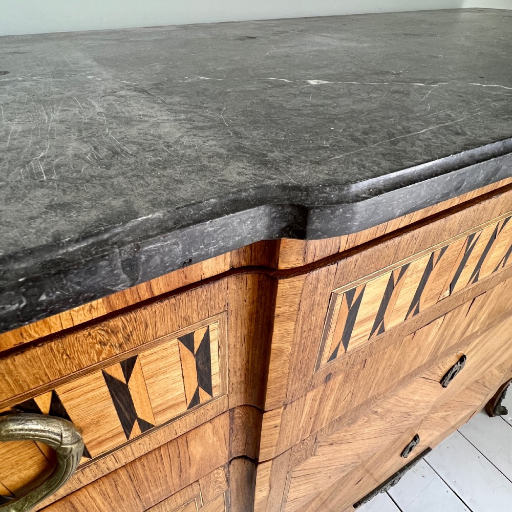 An antique Continental parquetry wooden commode featuring geometric wood inlays, brass ring handles, and a dark grey marble top. View VIII