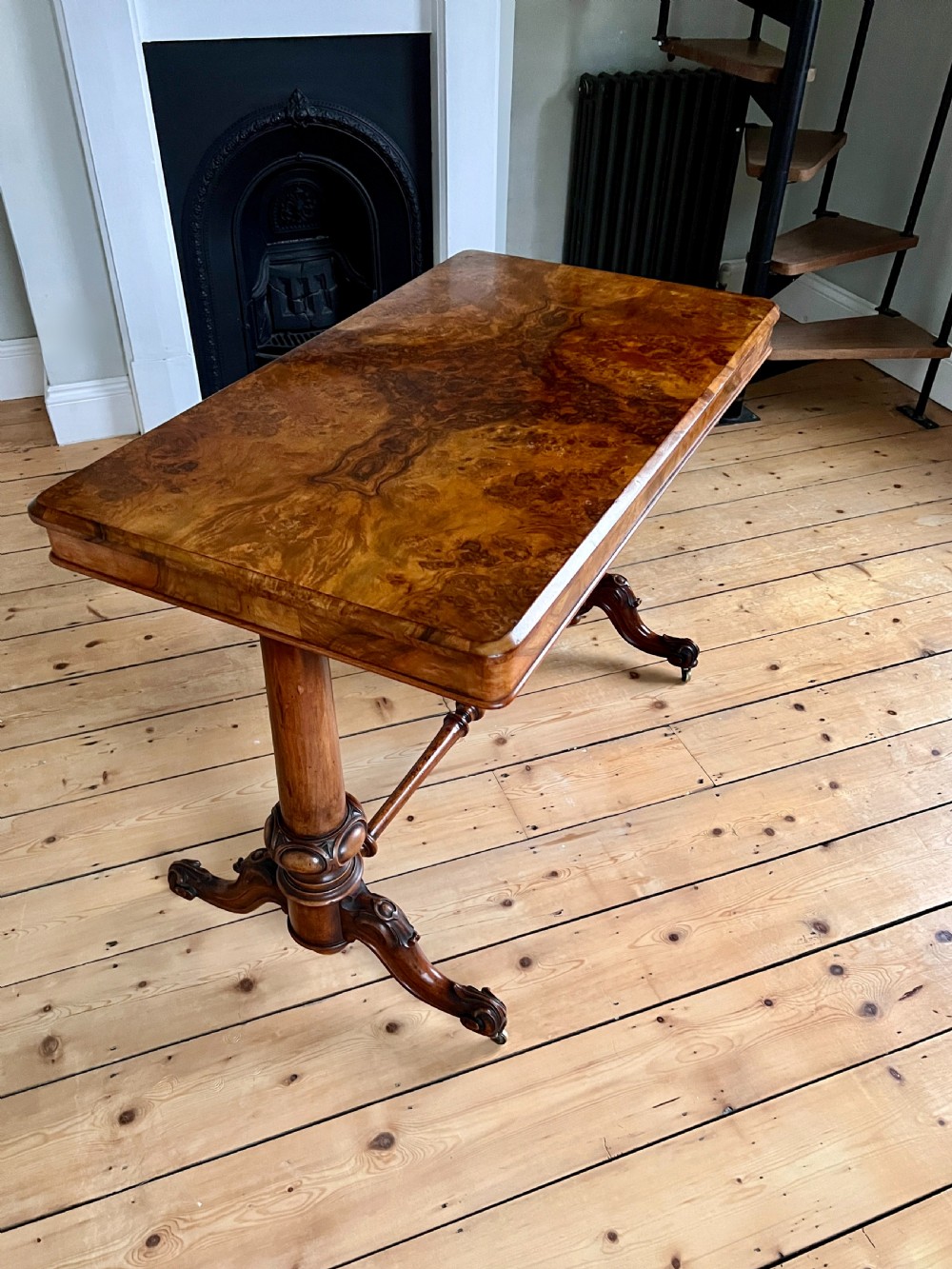 A Victorian burr walnut occasional table featuring a highly figured wood grain top, dual turned pedestals connected by a stretcher, and carved splayed legs on brass castors.