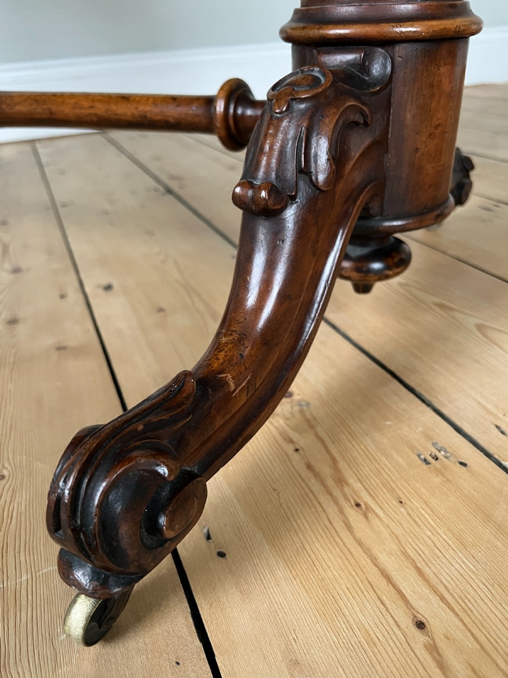 A Victorian burr walnut occasional table featuring a highly figured wood grain top, dual turned pedestals connected by a stretcher, and carved splayed legs on brass castors. View II