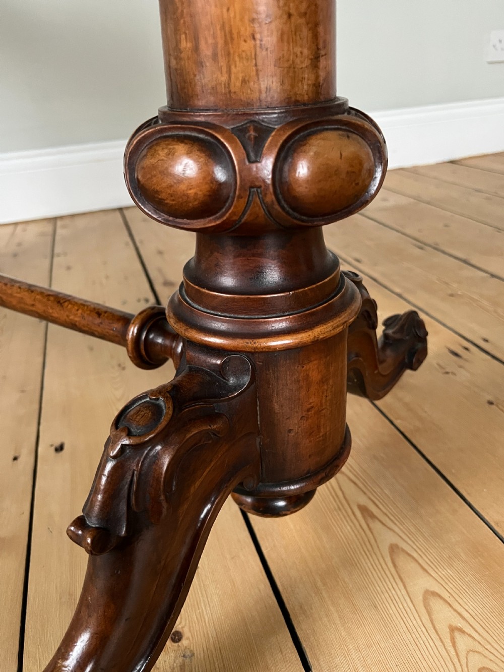 A Victorian burr walnut occasional table featuring a highly figured wood grain top, dual turned pedestals connected by a stretcher, and carved splayed legs on brass castors. View III