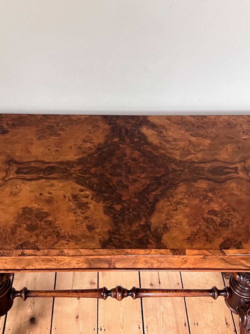 A Victorian burr walnut occasional table featuring a highly figured wood grain top, dual turned pedestals connected by a stretcher, and carved splayed legs on brass castors. View VIII