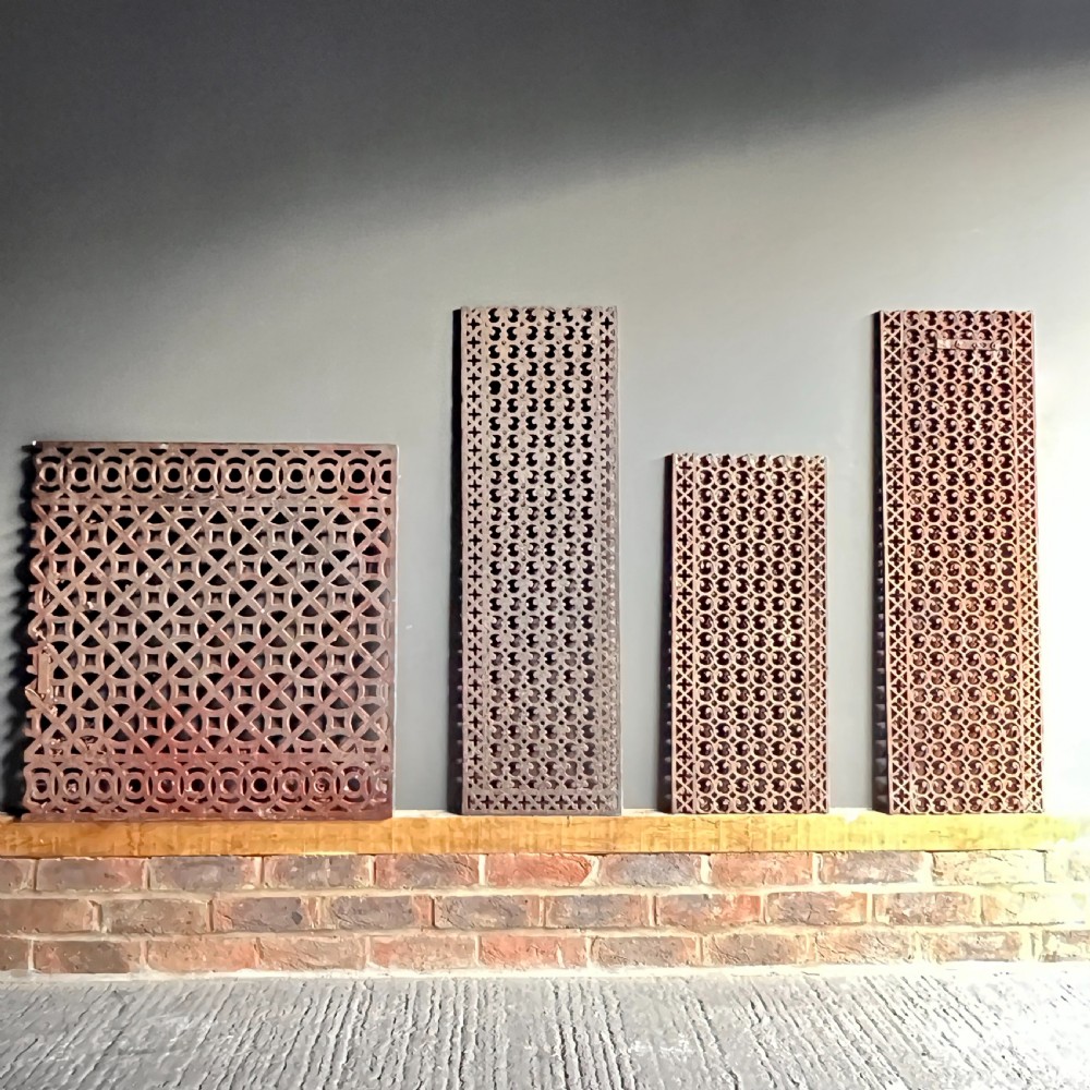 Four heavy rectangular cast iron architectural panels with pierced geometric openwork patterns and a weathered rust brown finish.
