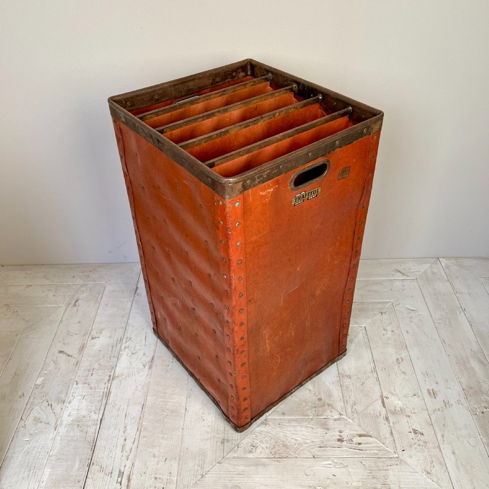 A pair of tall, terracotta-red industrial storage bins with metal-trimmed rims, riveted edges, cut-out side handles, and internal slots. View III