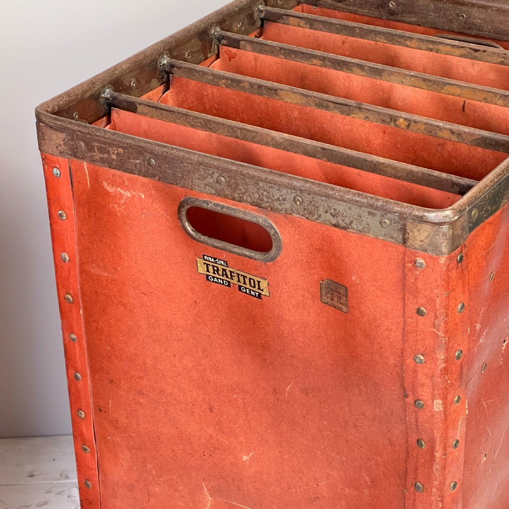 A pair of tall, terracotta-red industrial storage bins with metal-trimmed rims, riveted edges, cut-out side handles, and internal slots. View IV
