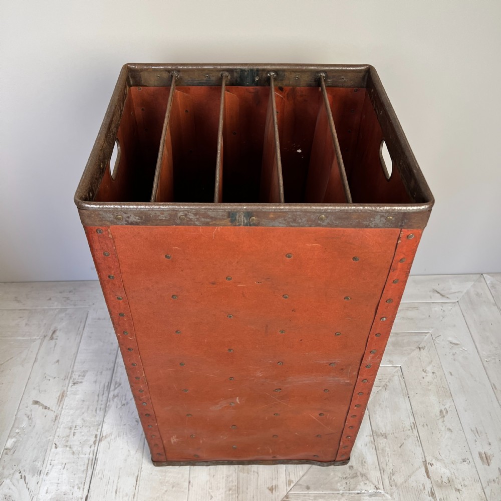 A pair of tall, terracotta-red industrial storage bins with metal-trimmed rims, riveted edges, cut-out side handles, and internal slots. View V