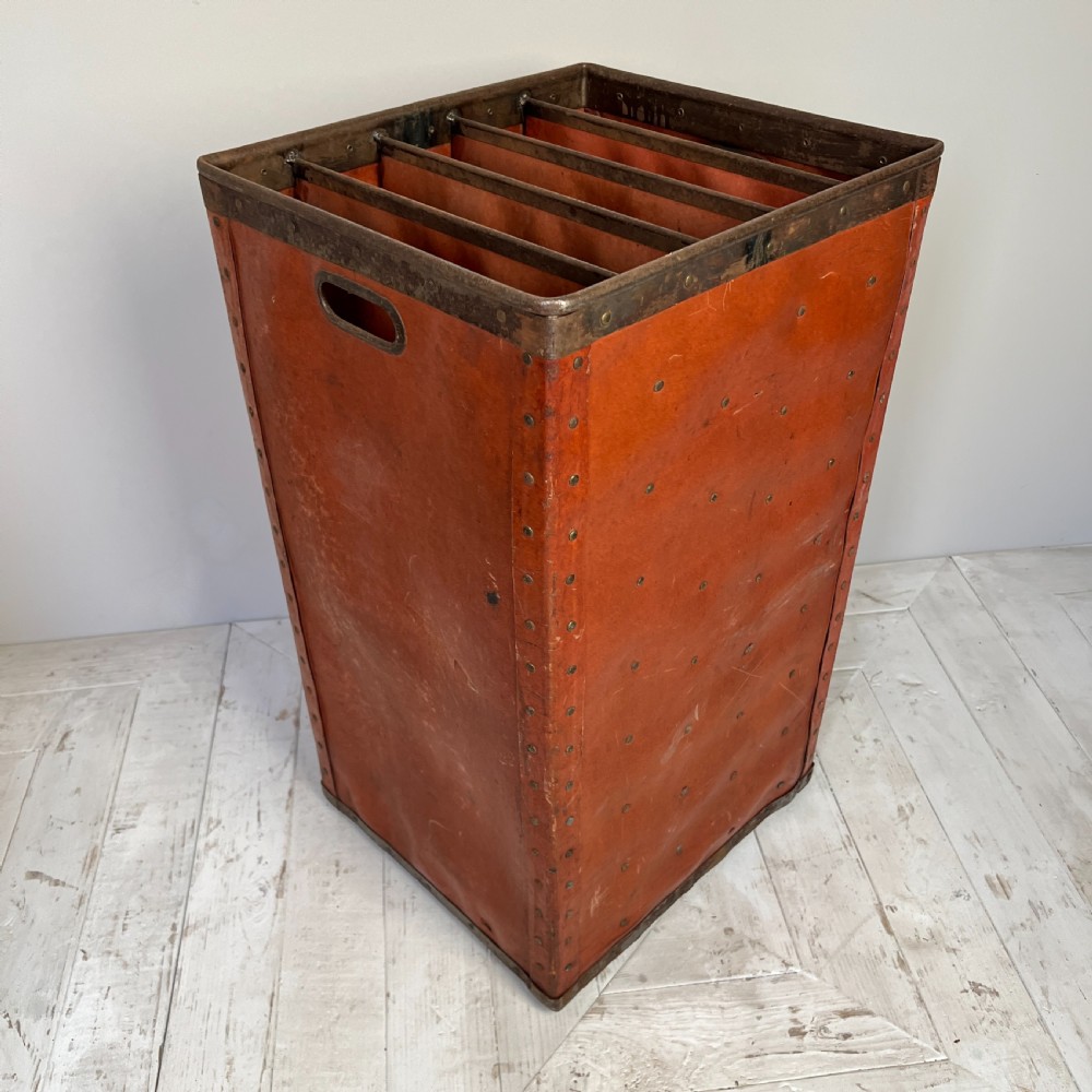 A pair of tall, terracotta-red industrial storage bins with metal-trimmed rims, riveted edges, cut-out side handles, and internal slots. View VI