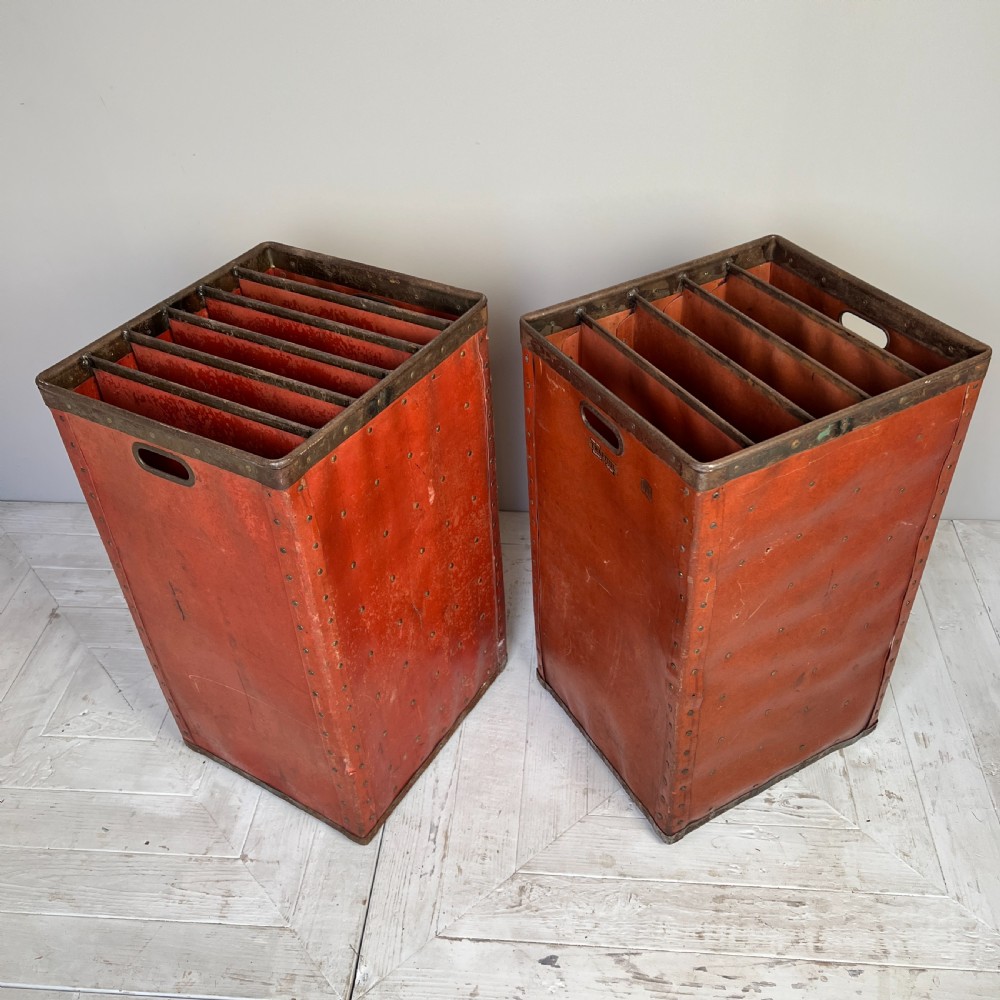 A pair of tall, terracotta-red industrial storage bins with metal-trimmed rims, riveted edges, cut-out side handles, and internal slots. View VII