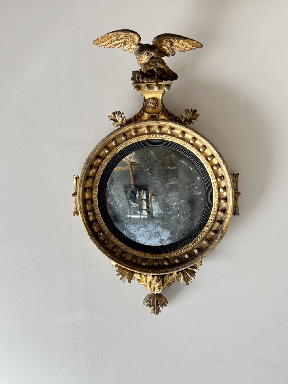 A circular Regency giltwood convex wall mirror topped with a carved eagle cresting and decorated with spherules along the frame.