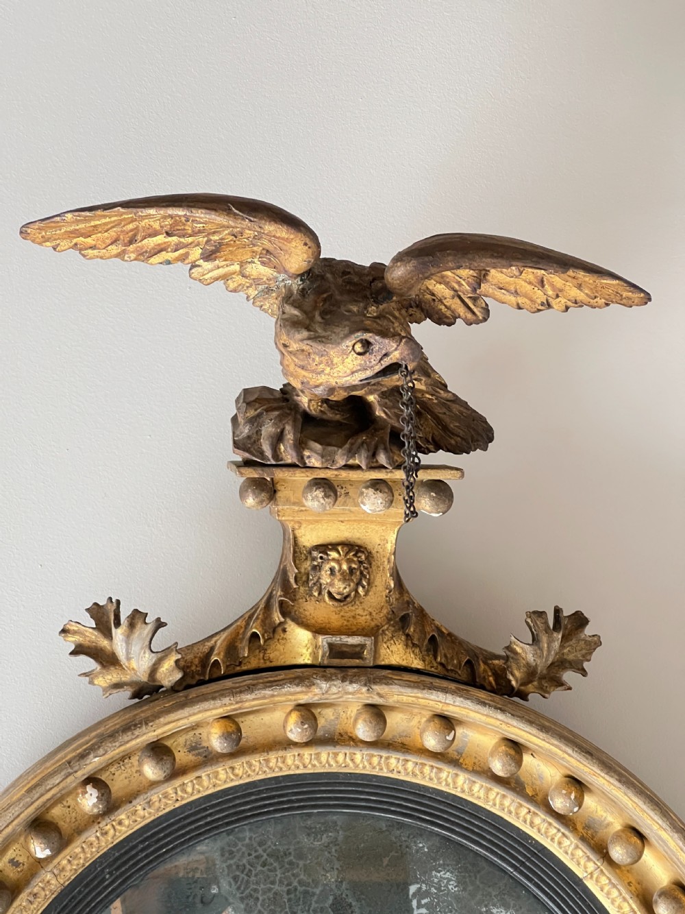 A circular Regency giltwood convex wall mirror topped with a carved eagle cresting and decorated with spherules along the frame. View II