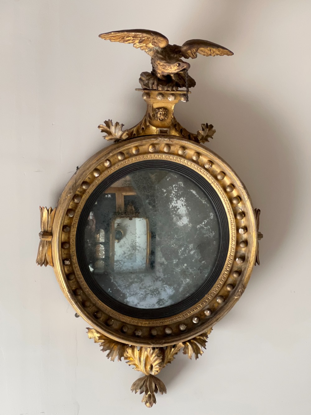 A circular Regency giltwood convex wall mirror topped with a carved eagle cresting and decorated with spherules along the frame. View III