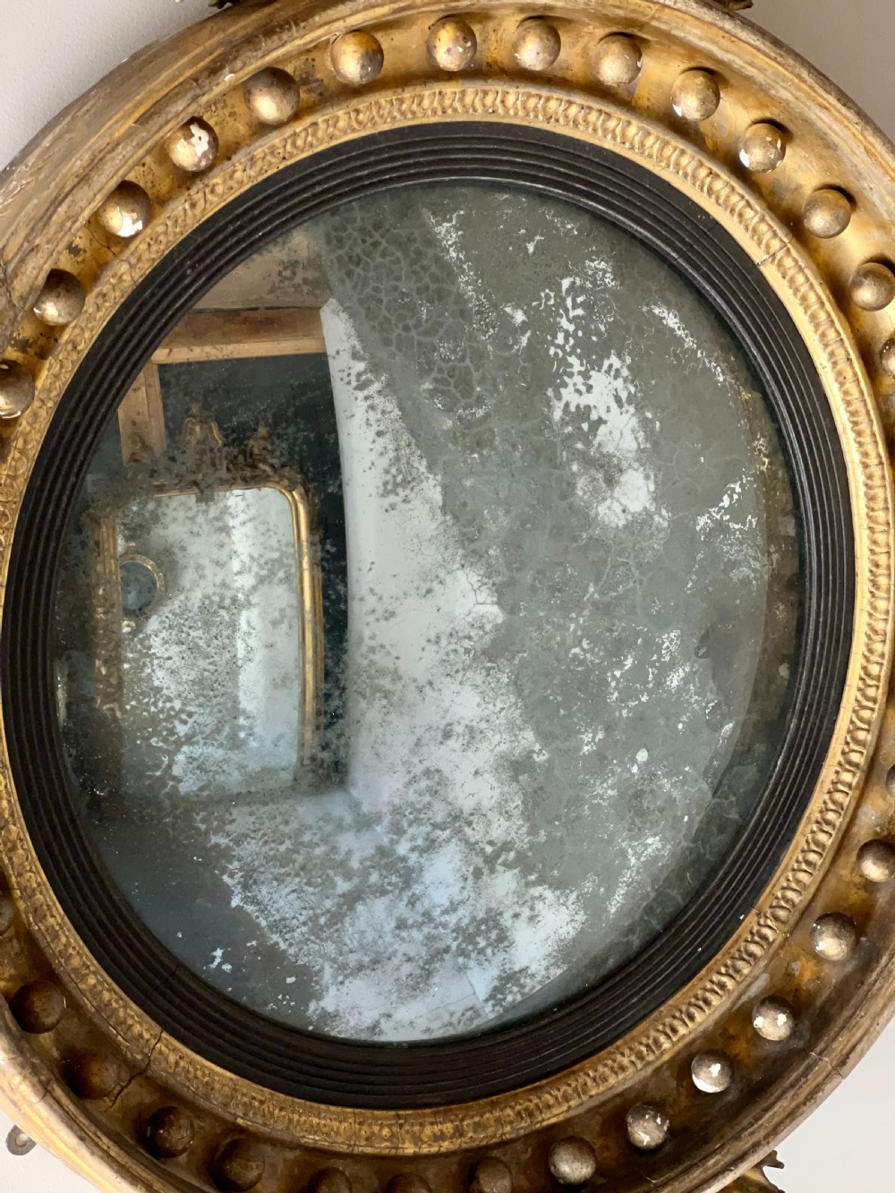 A circular Regency giltwood convex wall mirror topped with a carved eagle cresting and decorated with spherules along the frame. View V