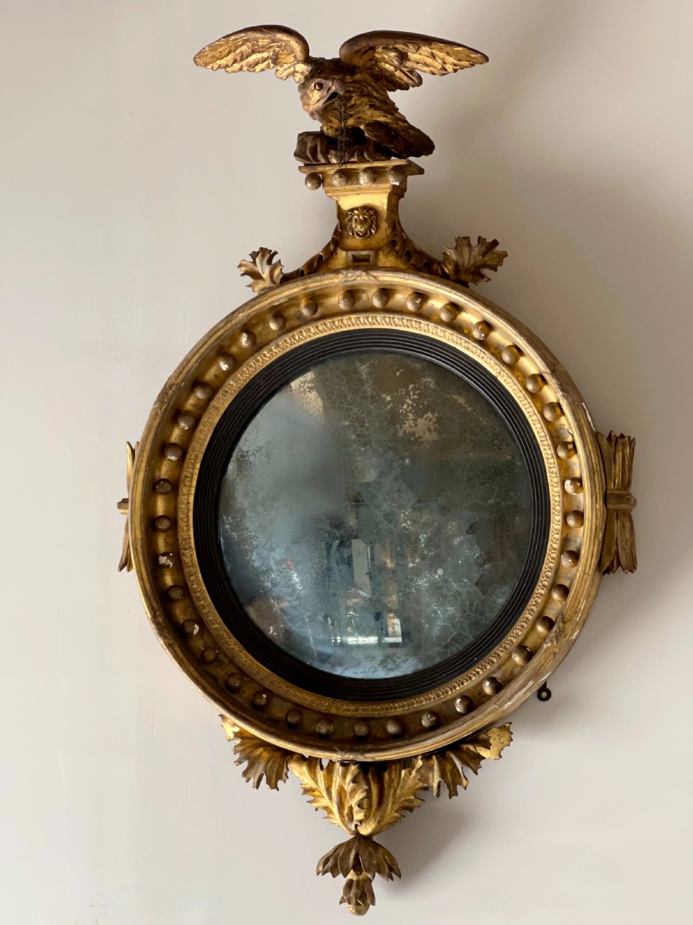 A circular Regency giltwood convex wall mirror topped with a carved eagle cresting and decorated with spherules along the frame. View VI